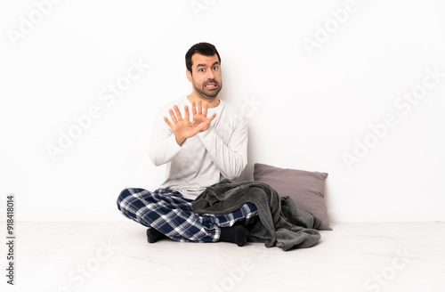 Caucasian man in pajamas sitting on the floor at indoors nervous stretching hands to the front