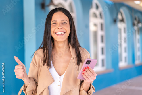 Wallpaper Mural Young woman at outdoors using mobile phone while doing thumbs up Torontodigital.ca