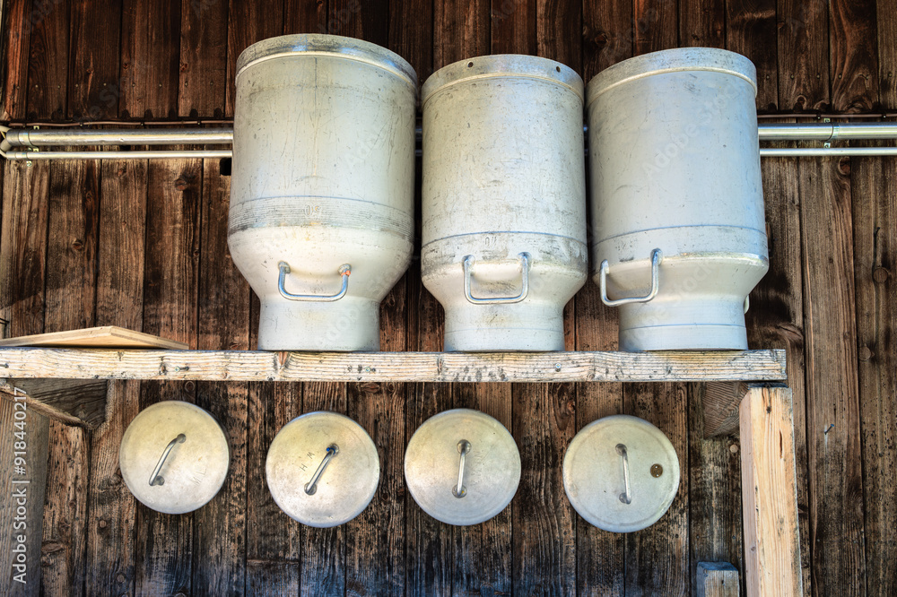 Stacked metal milk containers and covers hanging on wooden wall of alpine cottage. Stacked metal milk containers and covers hanging on wooden wall of alpine cottage.