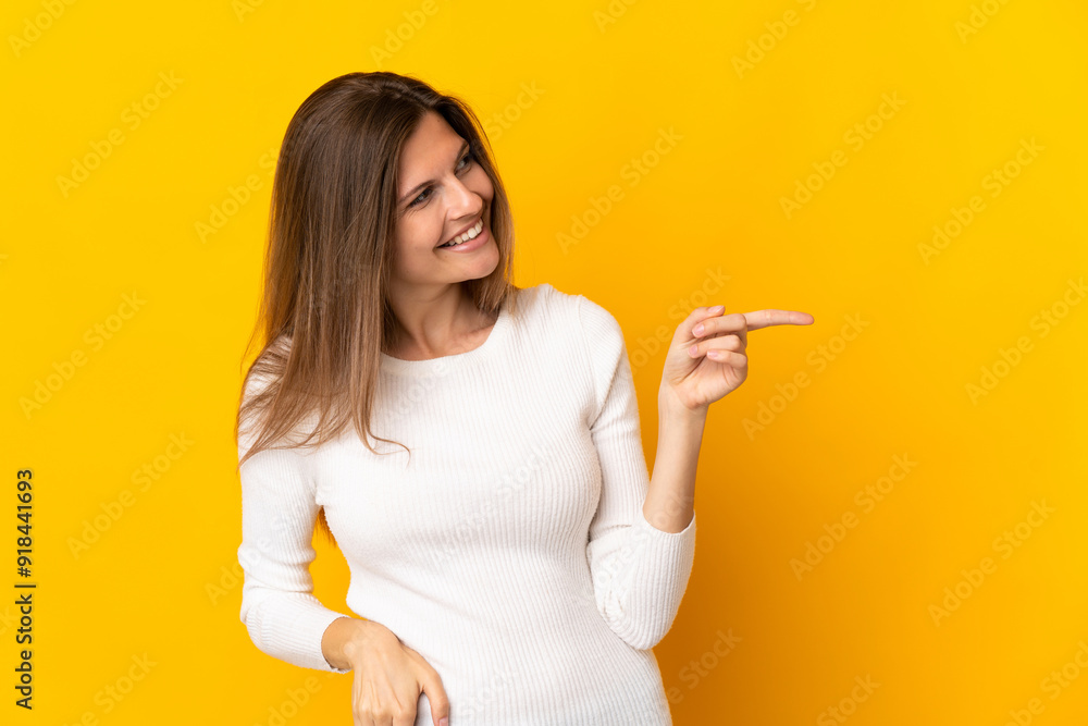 Young Slovak woman isolated on yellow background pointing finger to the side and presenting a product Young Slovak woman isolated on yellow background pointing finger to the side and presenting a product