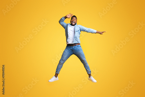 Unbelievable offer. Emotional afro guy jumping and pointing aside at copy space with hand, yellow background