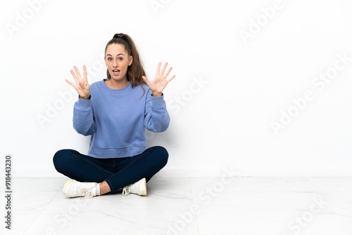 Young woman sitting on the floor counting nine with fingers photo