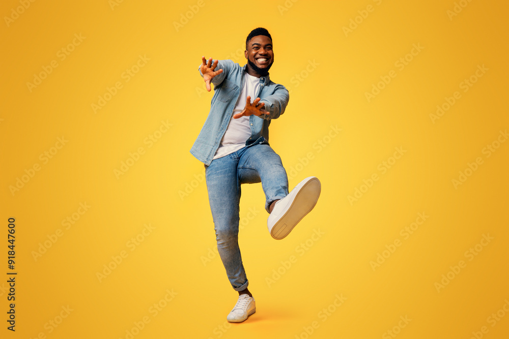 Funny african american guy dancing and extending his hands to camera over yellow studio background, low-angle view Funny african american guy dancing and extending his hands to camera over yellow studio background, low-angle view