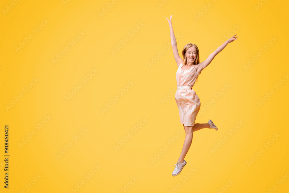 Obraz premium Freedom Of Youth. Portrait of carefree teen girl in summer dress jumping in the air with raised arms over yellow studio background, copy space