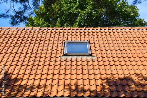 Attic skylight window on red ceramic tiles house roof.