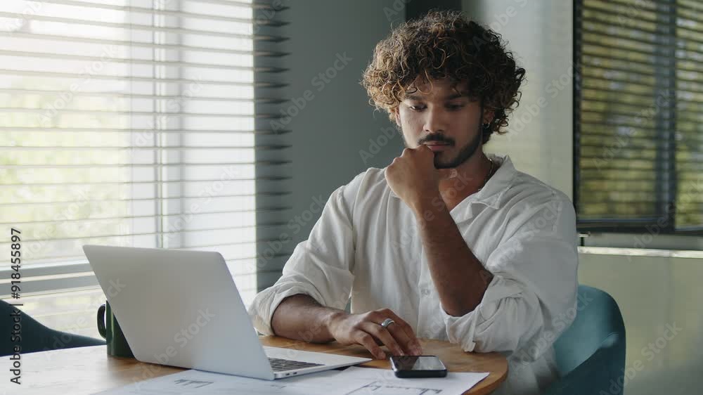 Young serious business man sits at table in home office, works with papers. Young serious business man sits at table in home office, works with papers.