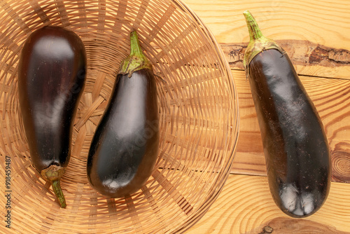 Three ripe eggplants in a basket on a wooden table, macro, top view.