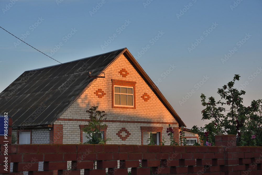 A brick house behind a red fence in the rays of the rising sun. Home in the morning. A brick house behind a red fence in the rays of the rising sun. Home in the morning.