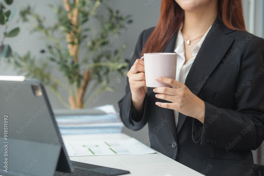 Businesswoman holding a cup of coffee while working on a laptop computer in the office Businesswoman holding a cup of coffee while working on a laptop computer in the office