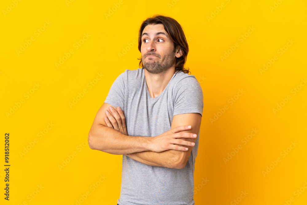 Young handsome man isolated on yellow background making doubts gesture while lifting the shoulders Young handsome man isolated on yellow background making doubts gesture while lifting the shoulders