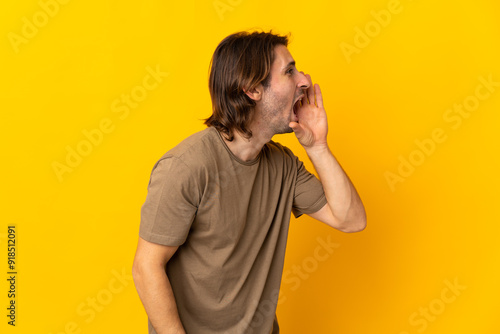 Young handsome man isolated on yellow background shouting with mouth wide open to the side