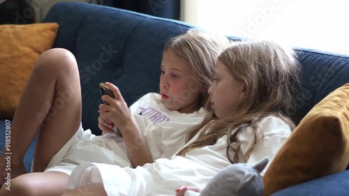 Elementary school girls stare intently at the smartphone screen. Child addiction. Gadgets in the modern world. Online communication on the Internet. Watching short videos, rils on social networks