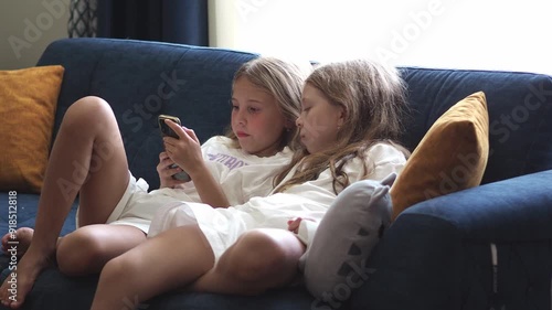 Elementary school girls stare intently at the smartphone screen. Child addiction. Gadgets in the modern world. Online communication on the Internet. Watching short videos, rils on social networks photo