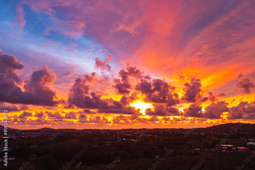 A breathtaking aerial view capturing a vibrant sunset over the Phuket countryside. The sky is ablaze with rich hues of yellow, orange, pink, and purple, while dramatic clouds float above the city A breathtaking aerial view capturing a vibrant sunset over the Phuket countryside. The sky is ablaze with rich hues of yellow, orange, pink, and purple, while dramatic clouds float above the city