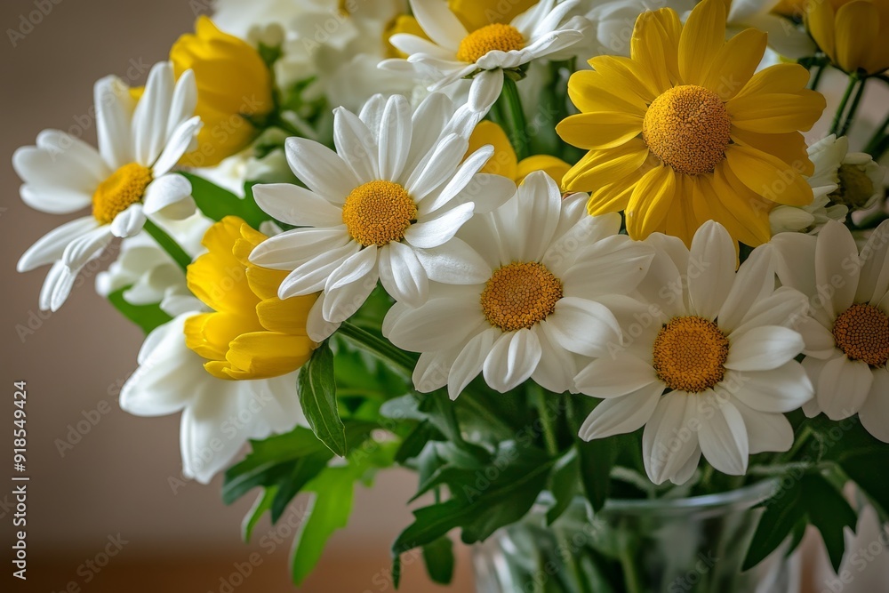 Fototapeta premium A stunning arrangement of white and yellow flowers fills a glass vase, adding a cheerful touch to the wooden table with their fresh and vibrant appearance
