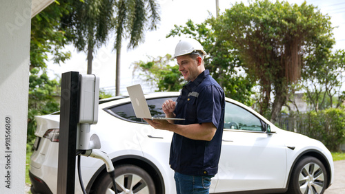 Qualified technician working on home EV charging station installation, making troubleshooting and configuration setup on charging system with laptop for EV at home. Synchronos photo