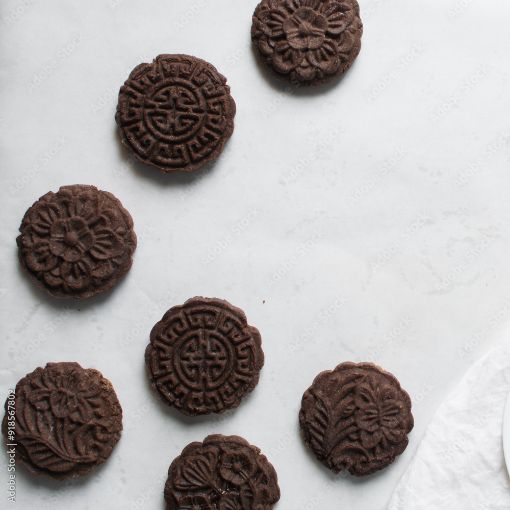 Overhead view of stamped chocolate cookies on a parchment lined baking tray, top view of embossed chocolate sugar cookies on a white background