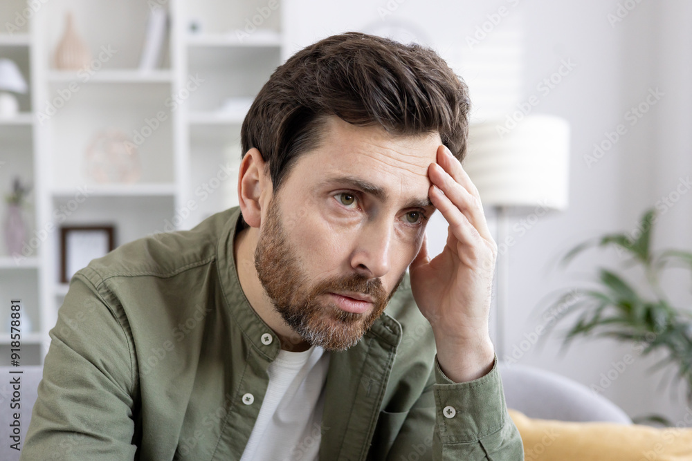 Man feeling stressed and worried at home holding head with hand. Image conveys stress, frustration, and contemplation indoors in casual clothing. Man feeling stressed and worried at home holding head with hand. Image conveys stress, frustration, and contemplation indoors in casual clothing.