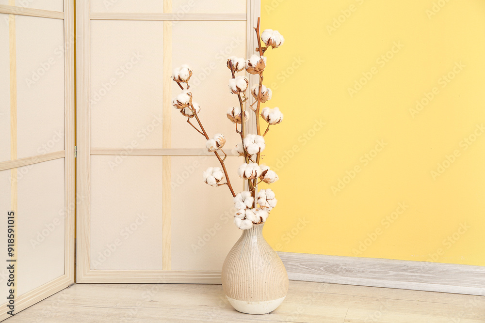 Vase of cotton sprigs on floor with dressing screen near yellow wall Vase of cotton sprigs on floor with dressing screen near yellow wall