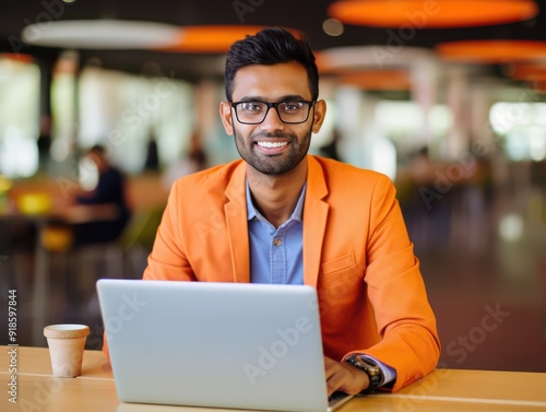 Happy Indian man in orange attire working on laptop indoors