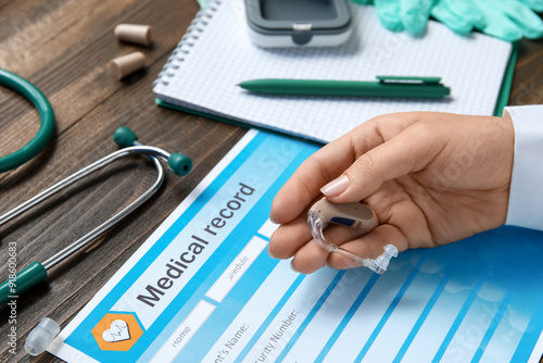 Hand of female doctor with hearing aid, medical record, notebook and pen on w...