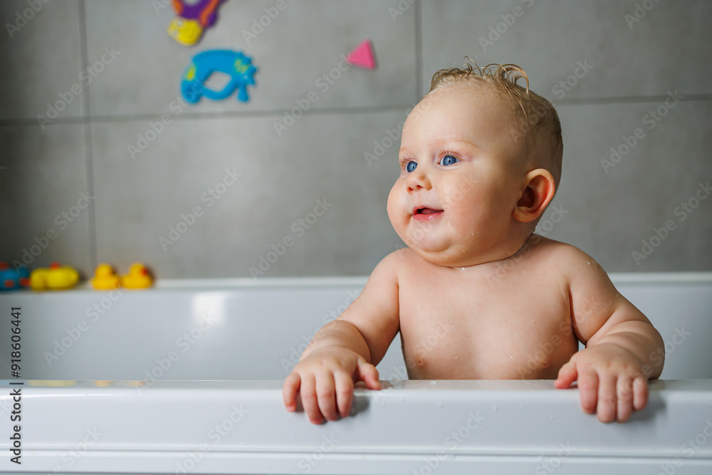A smiling baby is standing in a white bath with water. Baby bathing in water. Personal hygiene of the baby. A smiling baby is standing in a white bath with water. Baby bathing in water. Personal hygiene of the baby.