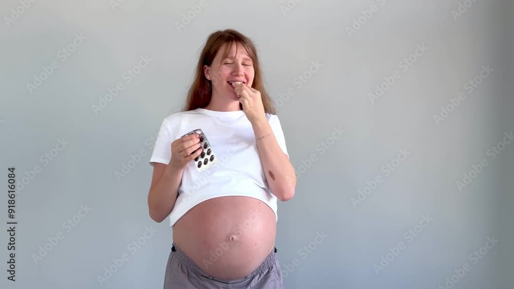 Young pregnant woman taking pills, capsules in hands and stroking her belly Young pregnant woman taking pills, capsules in hands and stroking her belly