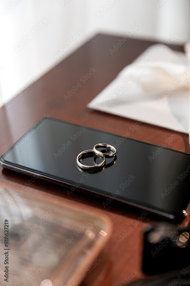 Groom's wedding essentials on table, featuring rings on phone, bow tie, boutonniere, perfume, belt Groom's wedding essentials on table, featuring rings on phone, bow tie, boutonniere, perfume, belt