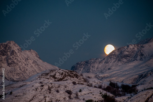 A near full moon is slowly creeping behind a mountain along the norwegian coast on an early winter morning near the town of Bodo. photo