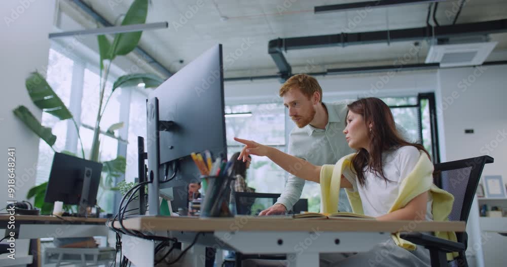 Side view of mixed-raced people speaking together in spacious office. Hardworking woman using computer while handsome manager standing next to her. Colleagues discussing about working questions. Side view of mixed-raced people speaking together in spacious office. Hardworking woman using computer while handsome manager standing next to her. Colleagues discussing about working questions.