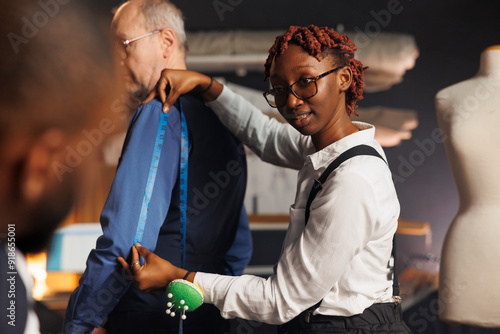 African american needleworker providing arm measurements to suitmaking craftsman in sartorial process. Skilled seamstress using tape to determine proper business suit sleave length photo