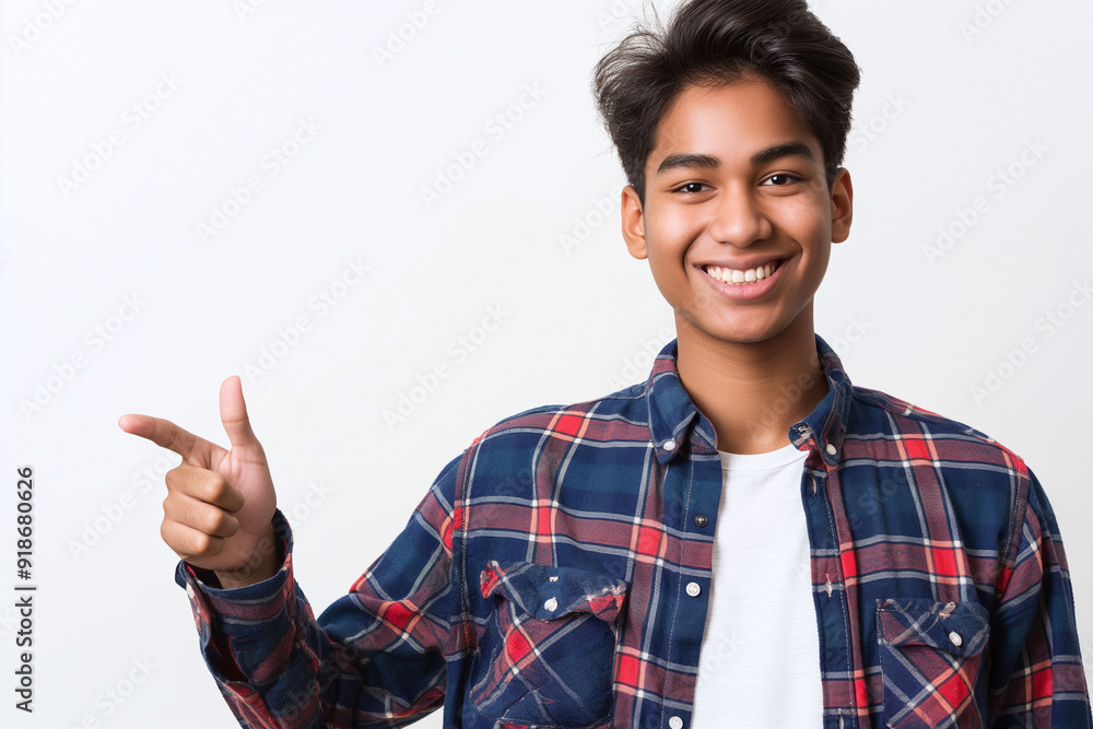 A young Indian student with a bright smile points to the side while wearing a casual plaid shirt, isolated on a white background