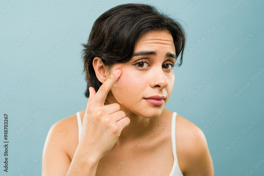 Hispanic woman with brown hair leaning in as if she was looking at herself on a mirror, against a blue background in a studio Hispanic woman with brown hair leaning in as if she was looking at herself on a mirror, against a blue background in a studio