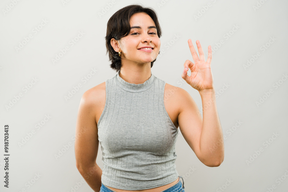 Portrait of a smiling young latina woman making an ok gesture against a white background Portrait of a smiling young latina woman making an ok gesture against a white background