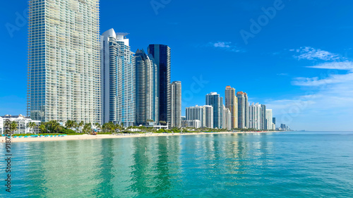Miami Sunny Isles Beach. Skyscrapers on bright sunny Florida summer day. Ocean with blue clear sky. Travel location for vacation with luxury architecture. City with sand beach and clear blue water.