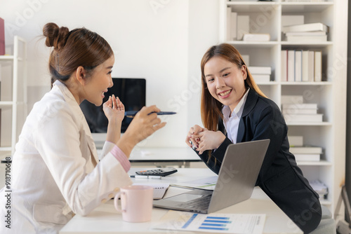 Two Asian businesswomen working together, meeting and discussing a new business project, creative team analyzing documents on marketing plan Laptop and documents on the table