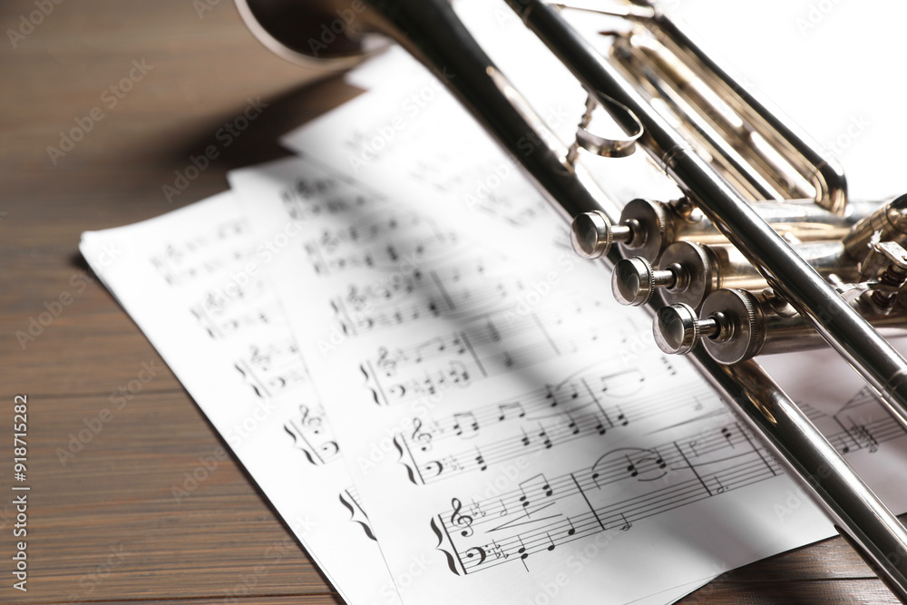 Obraz premium Trumpet and music sheet papers with notes on wooden table, closeup