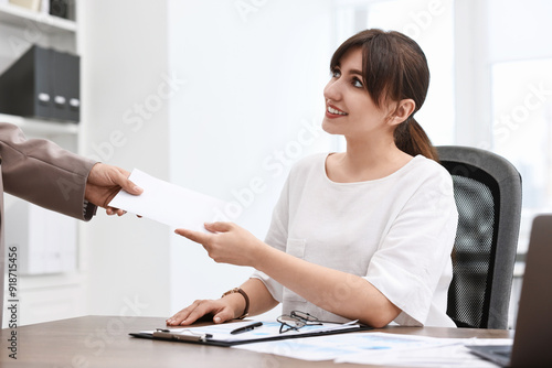Smiling employee receiving envelope with salary from boss in office