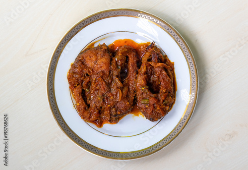 Spicy rui fish curry or rui mach bhuna in a white plate on light wooden surface.