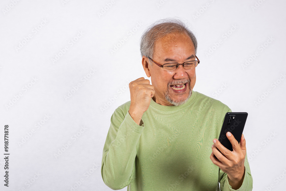 Portrait Asian smiling old man holding a cell phone celebrating something on the phone studio shot isolated on white background, happy senior man doing winner gesture celebrate on mobile phone Portrait Asian smiling old man holding a cell phone celebrating something on the phone studio shot isolated on white background, happy senior man doing winner gesture celebrate on mobile phone