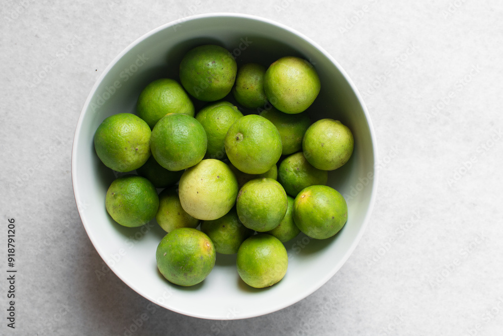 Overhead view of green limes in a white ceramic bowl, top view of organic limes in a white bowl Overhead view of green limes in a white ceramic bowl, top view of organic limes in a white bowl