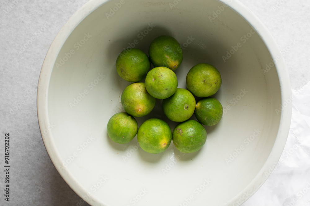 Overhead view of green limes in a white ceramic bowl, top view of organic limes in a white bowl Overhead view of green limes in a white ceramic bowl, top view of organic limes in a white bowl