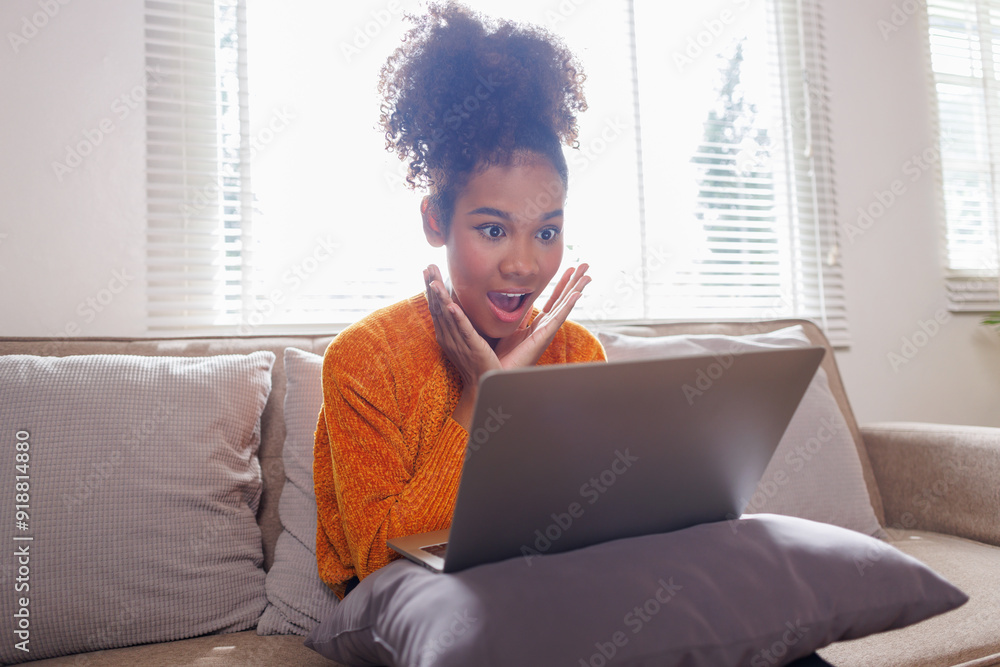Image of cheerful excited happy african american woman afro hair, using laptop while sitting on chair in living room Image of cheerful excited happy african american woman afro hair, using laptop while sitting on chair in living room