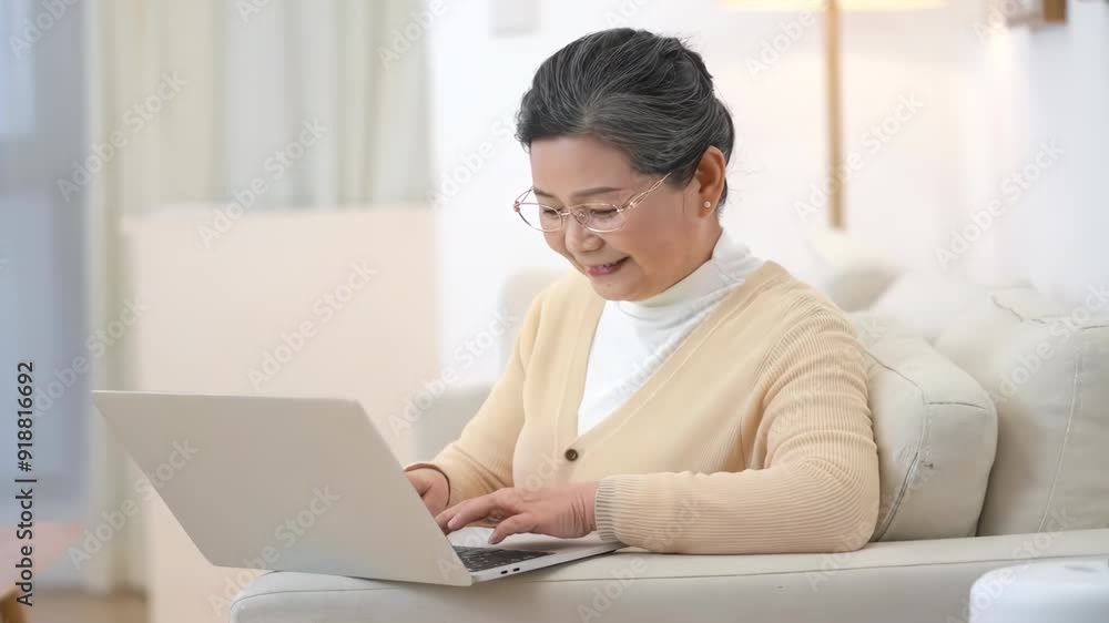 Senior elderly woman with glasses uses laptop to type on sofa in cozy living room to communicate and entertain in their home life. Adult female enjoying technology and communication. Senior elderly woman with glasses uses laptop to type on sofa in cozy living room to communicate and entertain in their home life. Adult female enjoying technology and communication.