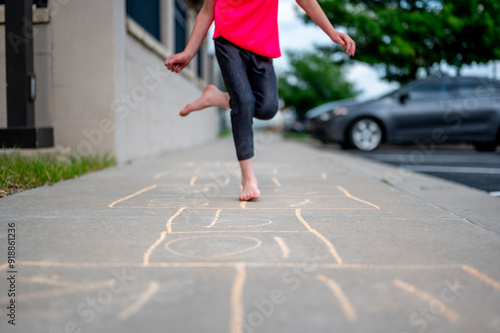 Selective focus on chalk numbers with a girl playing hop-scotch barefoot