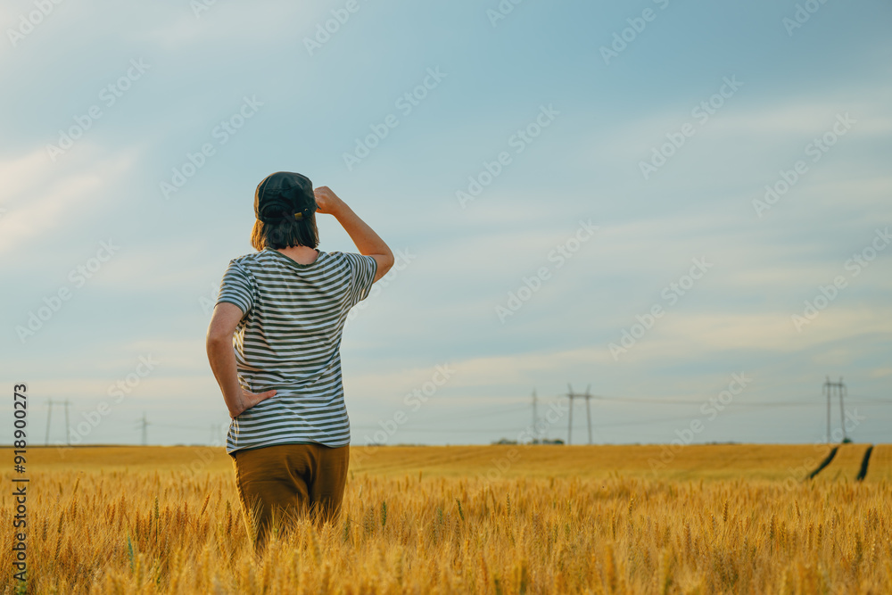 Female farmer standing in ripe wheat field and looking over the harvest ...