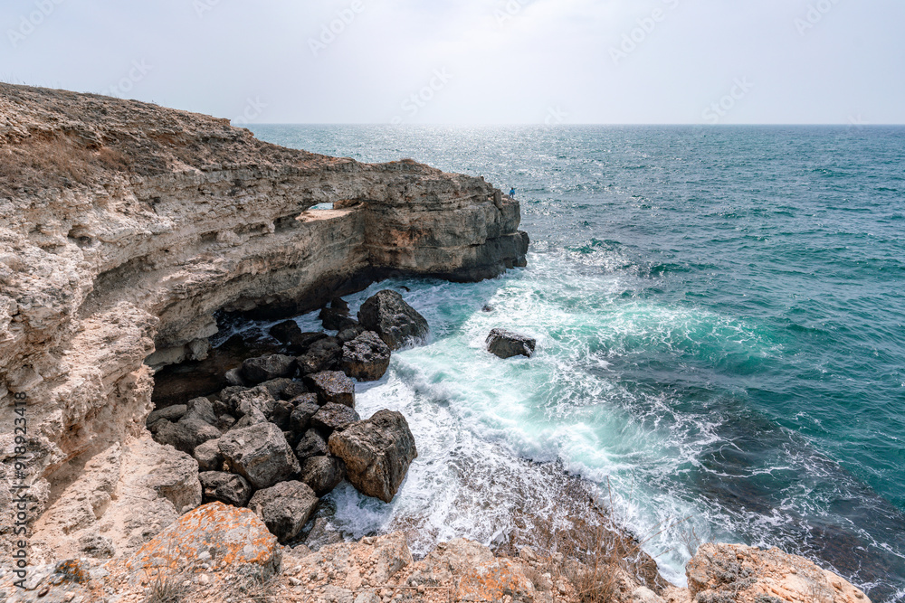 The ocean is calm and the sky is cloudy. The water is a deep blue color. The rocks are jagged and the waves are small. The ocean is calm and the sky is cloudy. The water is a deep blue color. The rocks are jagged and the waves are small.