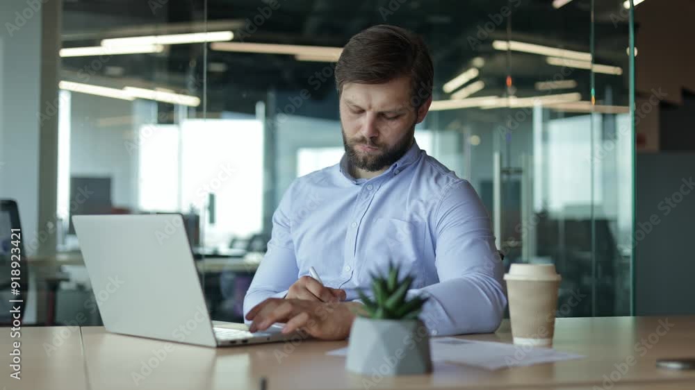 Serious businessman diligently working on laptop in a modern office environment Serious businessman diligently working on laptop in a modern office environment