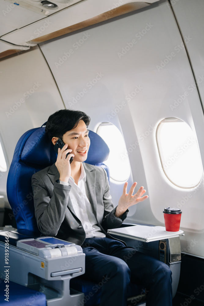Asian businessman or entrepreneur in a formal suit on an airplane sitting in business class using a phone, computer laptop Asian businessman or entrepreneur in a formal suit on an airplane sitting in business class using a phone, computer laptop