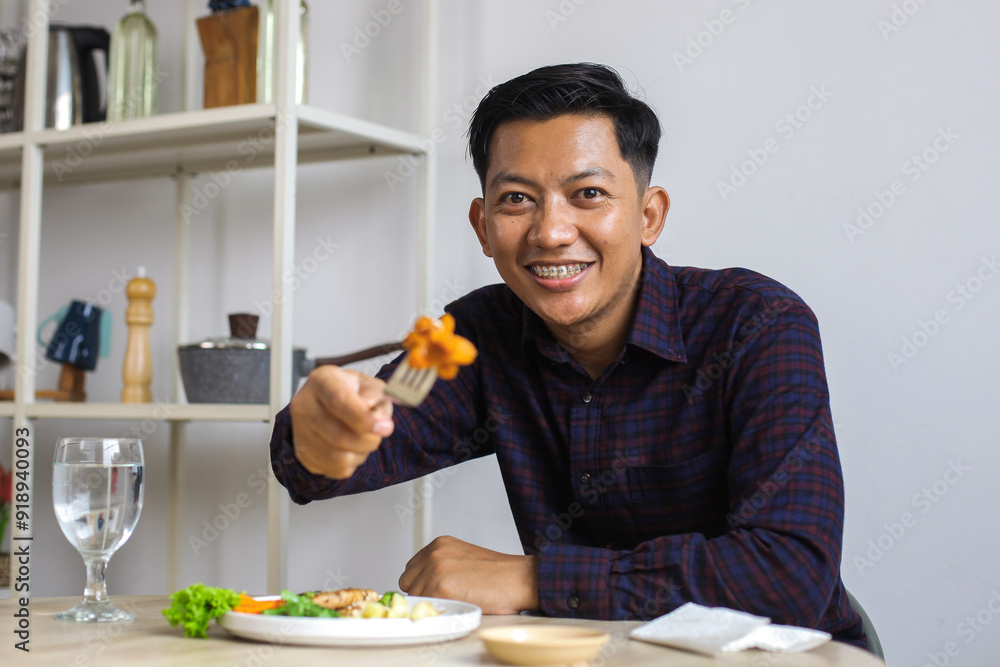 Happy Asian Man With Braces Wear Casual Holding Fork While Eating Sausage Happy Asian Man With Braces Wear Casual Holding Fork While Eating Sausage